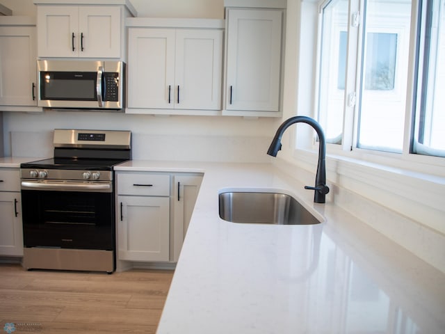 kitchen with white cabinets, sink, stainless steel appliances, and light hardwood / wood-style floors