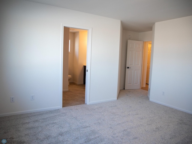 unfurnished bedroom featuring light colored carpet and ensuite bathroom