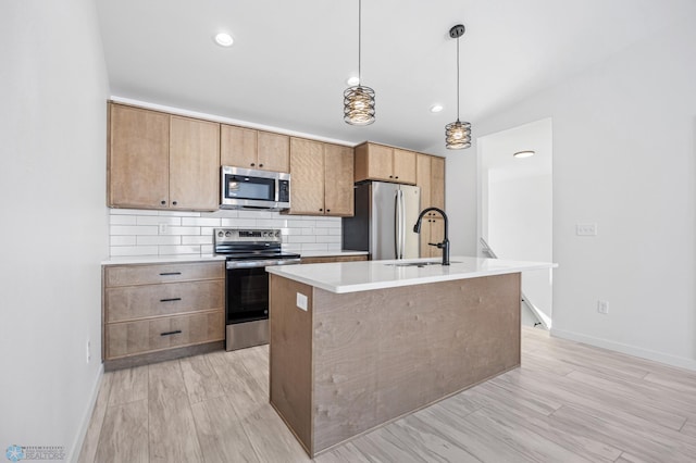 kitchen with pendant lighting, light countertops, appliances with stainless steel finishes, a sink, and an island with sink