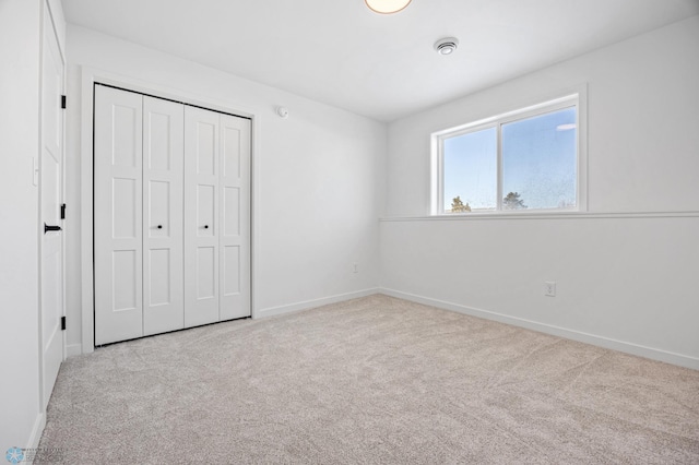 unfurnished bedroom with a closet, light carpet, and baseboards