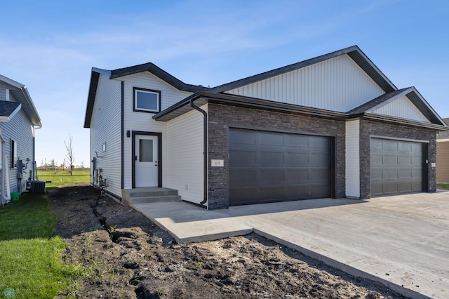 69 Cedar Dr, Mapleton, ND 58059 - view of front facade with an attached garage, concrete driveway, stone siding, cooling unit, and board and batten siding