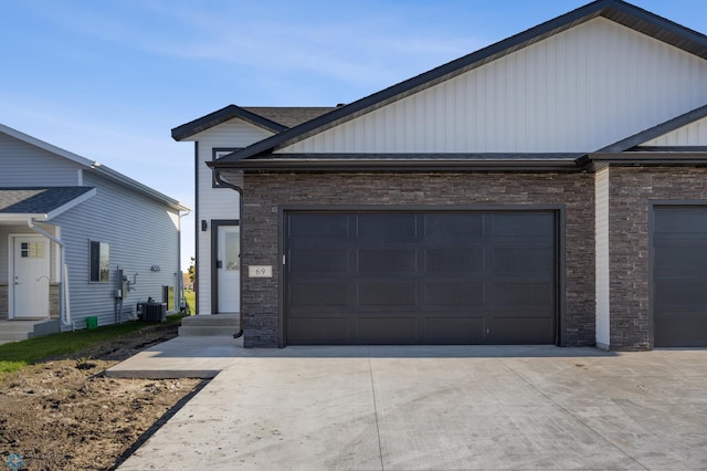 69 Cedar Dr, Mapleton, ND 58059 - view of front facade featuring board and batten siding, stone siding, driveway, central AC unit, and an attached garage