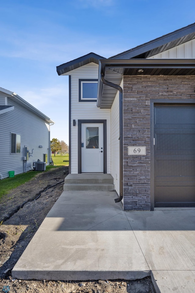 69 Cedar Dr, Mapleton, ND 58059 - view of exterior entry with central AC unit, stone siding, and a garage