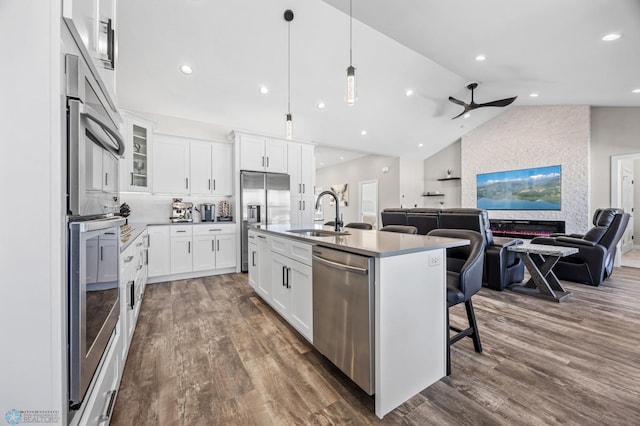 kitchen with an island with sink, appliances with stainless steel finishes, open floor plan, white cabinetry, and a sink