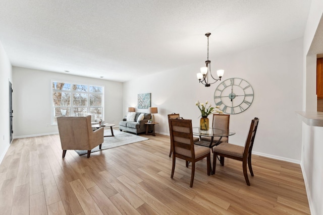 dining area featuring light hardwood / wood-style floors, a textured ceiling, and a notable chandelier