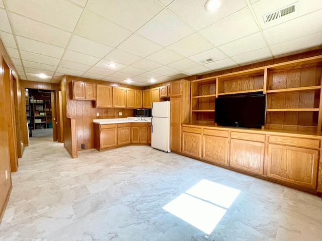 kitchen with built in shelves, a paneled ceiling, wood walls, and white fridge