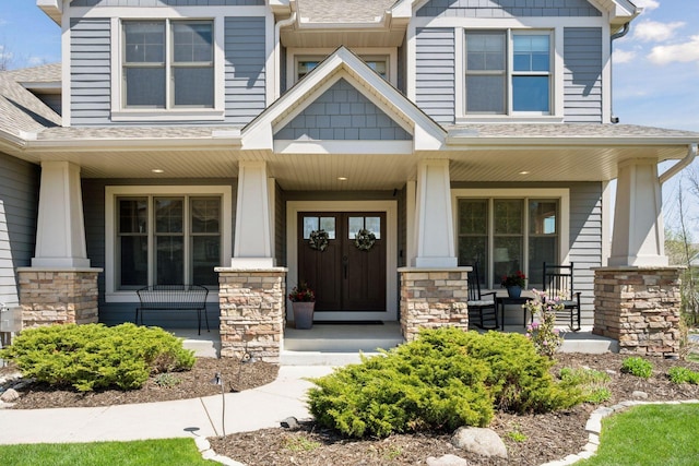 entrance to property with covered porch, stone siding, and roof with shingles