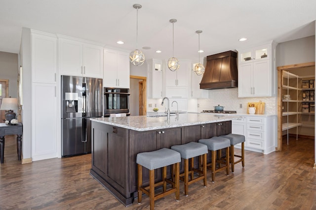 kitchen featuring dark wood-style flooring, appliances with stainless steel finishes, white cabinets, glass insert cabinets, and custom range hood