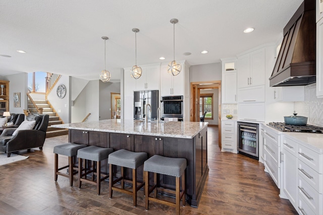 kitchen featuring custom exhaust hood, beverage cooler, open floor plan, gas cooktop, and stainless steel fridge with ice dispenser