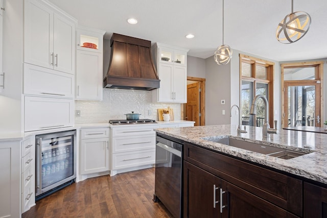 kitchen with appliances with stainless steel finishes, a sink, custom range hood, wine cooler, and glass insert cabinets