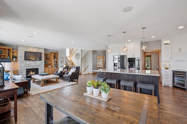 dining room with dark wood-style flooring, wine cooler, a stone fireplace, stairway, and recessed lighting