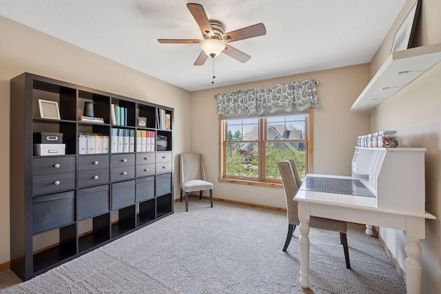 carpeted office space featuring a ceiling fan and baseboards