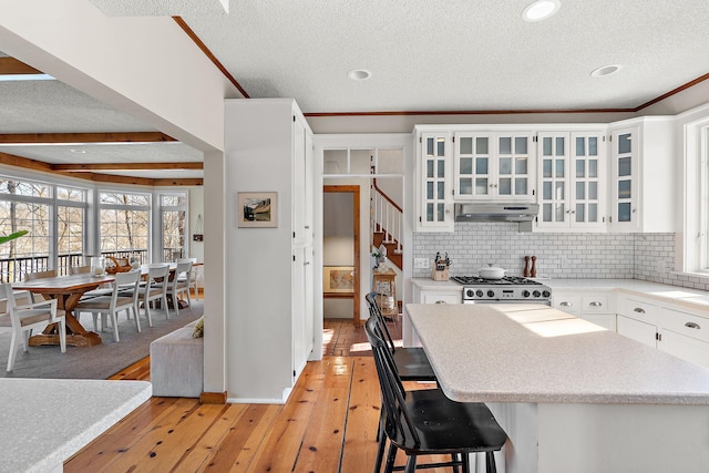 kitchen featuring white cabinets, glass insert cabinets, a breakfast bar, stove, and light countertops