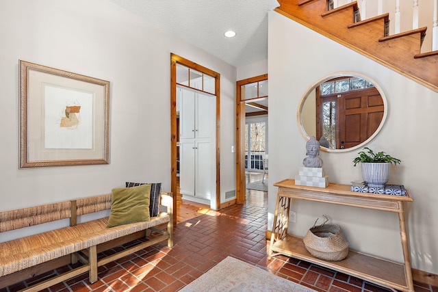 foyer with a textured ceiling, brick floor, recessed lighting, visible vents, and baseboards