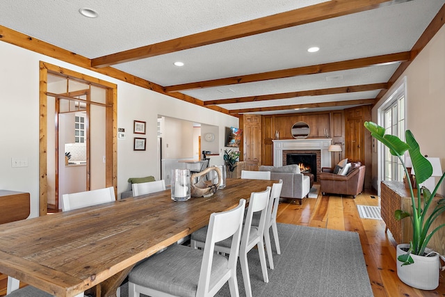 dining space with beamed ceiling, a textured ceiling, light wood-style floors, a fireplace, and recessed lighting