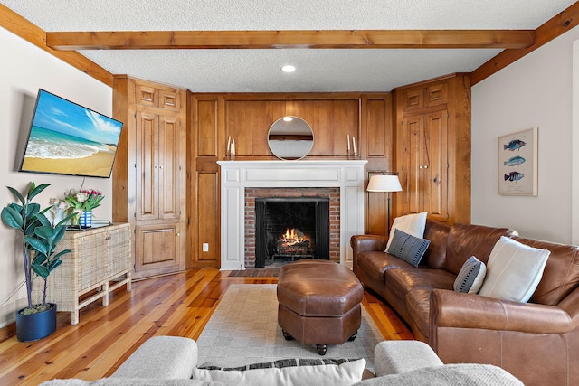 living room with beam ceiling, recessed lighting, a brick fireplace, a textured ceiling, and light wood-type flooring