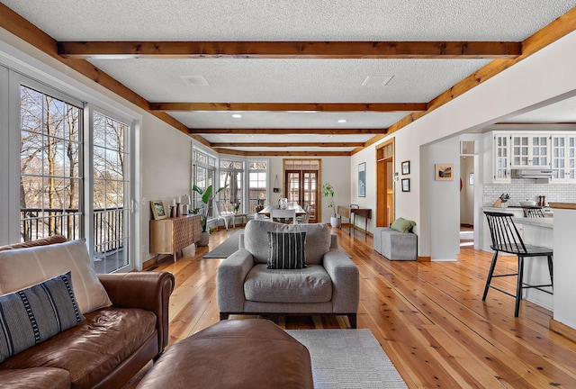 living area featuring light wood finished floors, baseboards, a textured ceiling, and beamed ceiling