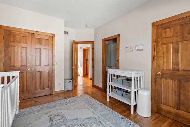 bedroom with a textured ceiling, wood finished floors, visible vents, and baseboards