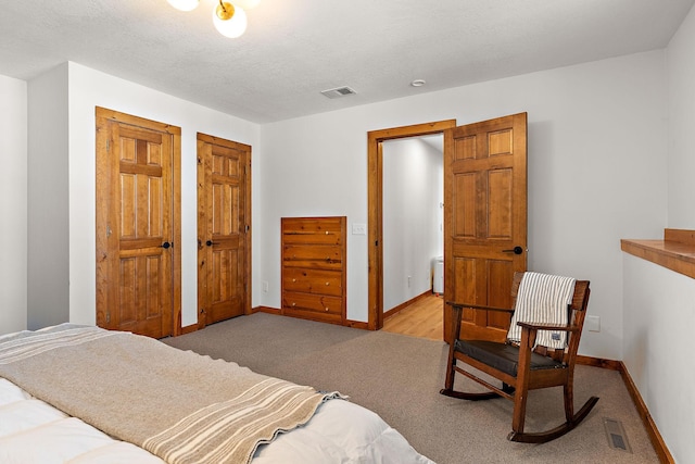 bedroom featuring multiple closets, visible vents, light carpet, and baseboards