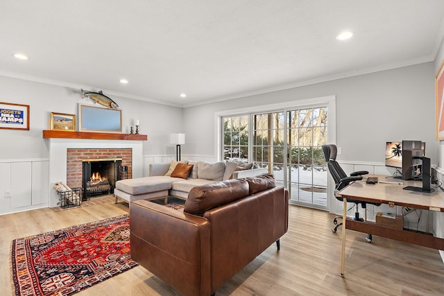 living room with ornamental molding, a brick fireplace, wainscoting, and light wood-style floors