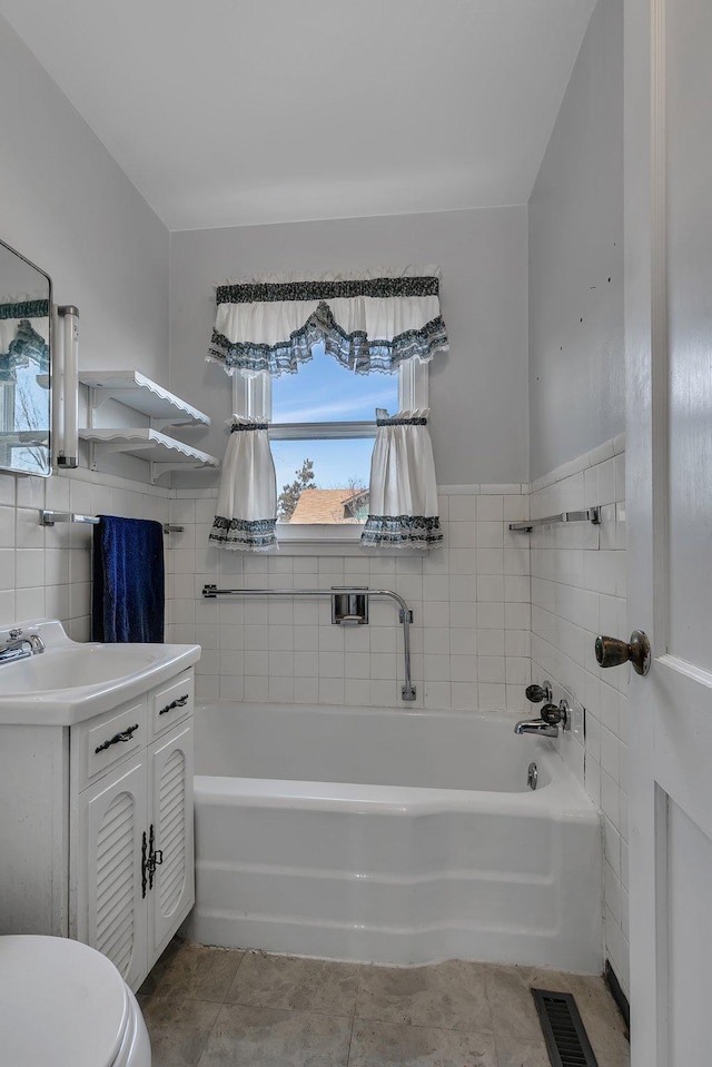 full bathroom with vanity, tile walls, a bath, and visible vents