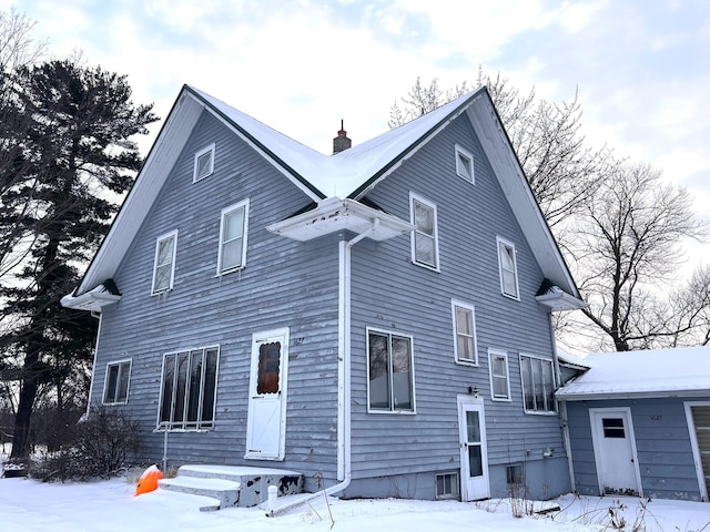 snow covered back of property featuring a chimney