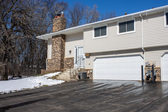 view of front of home with brick siding, a chimney, entry steps, a garage, and cooling unit