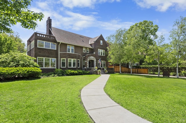 view of front of home featuring brick siding, a chimney, a front lawn, and fence