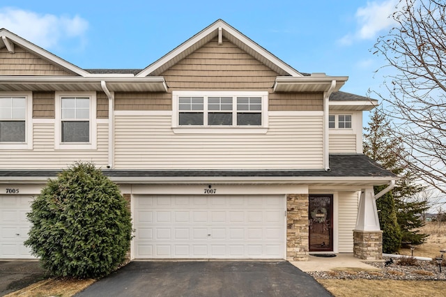 multi unit property featuring a garage, stone siding, roof with shingles, and aphalt driveway