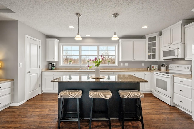 kitchen with white appliances, a breakfast bar, dark wood finished floors, and white cabinets