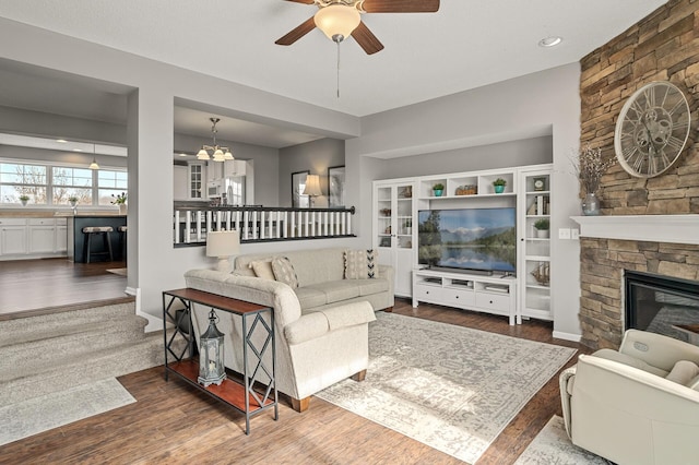 living room featuring a stone fireplace, ceiling fan with notable chandelier, and wood finished floors