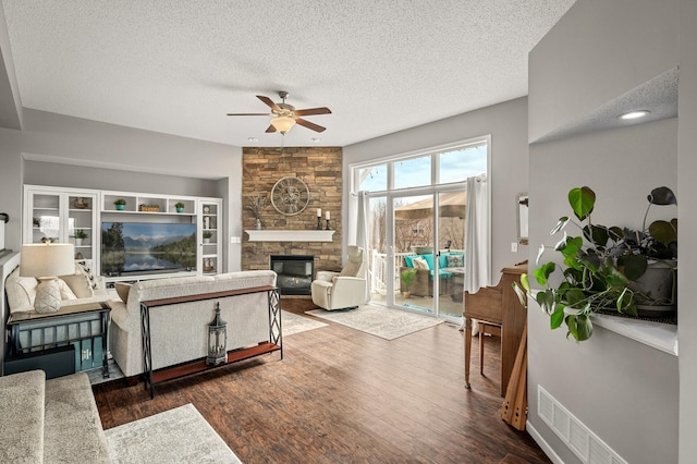 living area featuring a ceiling fan, visible vents, a fireplace, dark wood-style flooring, and a textured ceiling