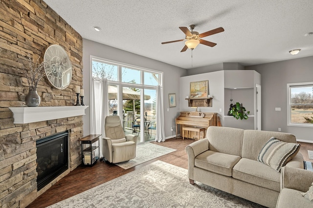 living area featuring a stone fireplace, wood finished floors, a wealth of natural light, and ceiling fan