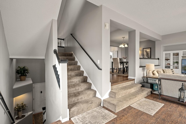 stairway featuring baseboards, a textured ceiling, an inviting chandelier, and wood finished floors