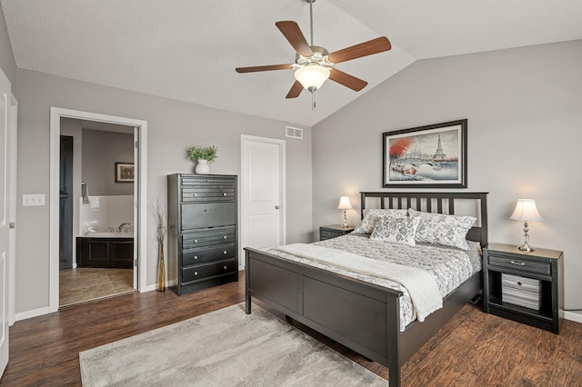 bedroom featuring wood finished floors, visible vents, baseboards, ensuite bath, and vaulted ceiling