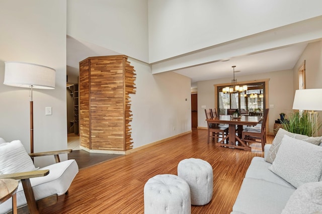 living area with an inviting chandelier, a high ceiling, baseboards, and wood finished floors