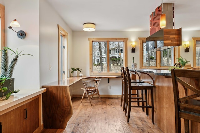 kitchen featuring light wood finished floors, baseboards, built in study area, a breakfast bar area, and brown cabinets