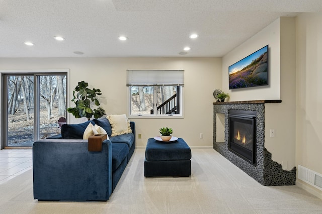 carpeted living area featuring a textured ceiling, a glass covered fireplace, visible vents, and recessed lighting