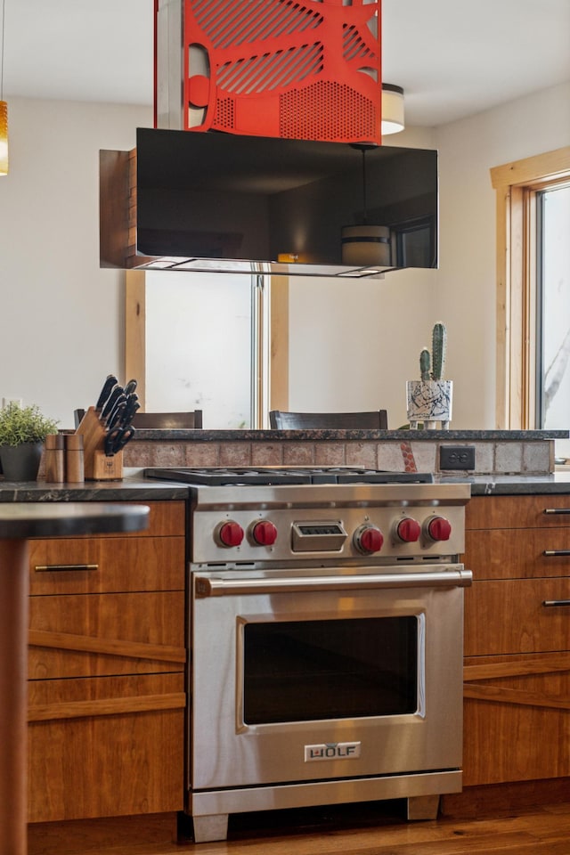 kitchen with dark countertops, brown cabinets, wood finished floors, premium range, and ventilation hood