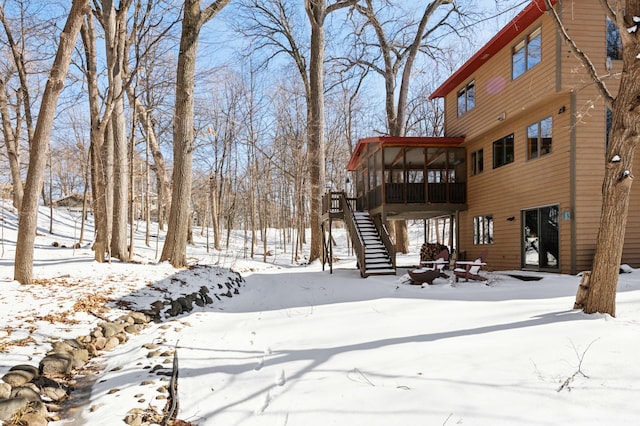 snow covered house featuring an outdoor fire pit, stairway, a wooden deck, and a sunroom