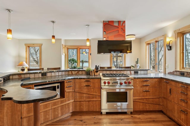 kitchen featuring brown cabinets, decorative light fixtures, appliances with stainless steel finishes, and hardwood / wood-style flooring