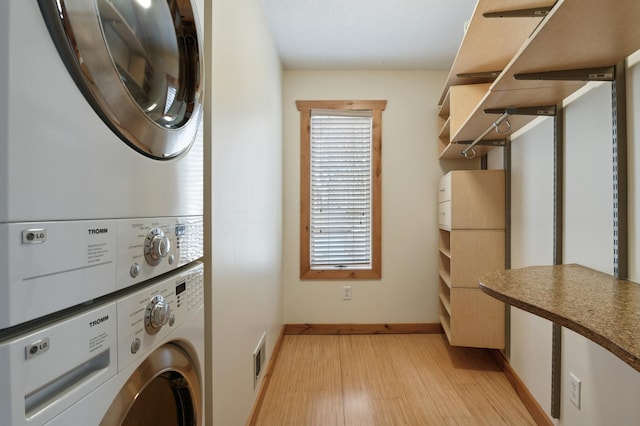 laundry room featuring light wood-style floors, baseboards, stacked washer and clothes dryer, and visible vents