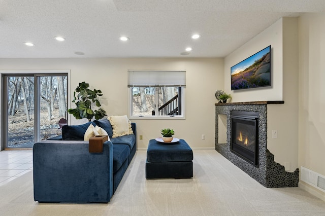 carpeted living area with visible vents, recessed lighting, a textured ceiling, and a glass covered fireplace