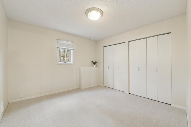 unfurnished bedroom featuring two closets, a textured ceiling, baseboards, and light colored carpet