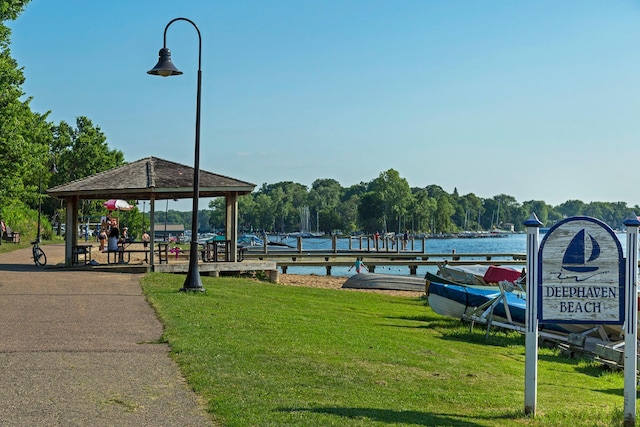 view of property's community with a lawn, a water view, a gazebo, and a boat dock