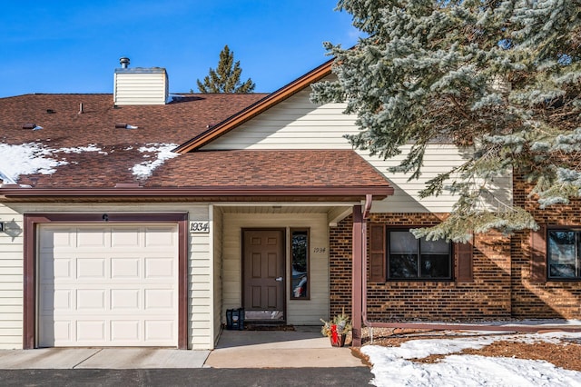 multi unit property featuring a garage, roof with shingles, a chimney, and brick siding