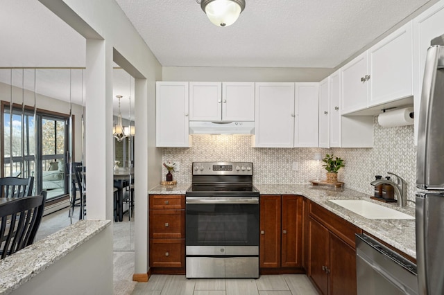 kitchen featuring a sink, light stone counters, under cabinet range hood, stainless steel appliances, and decorative backsplash