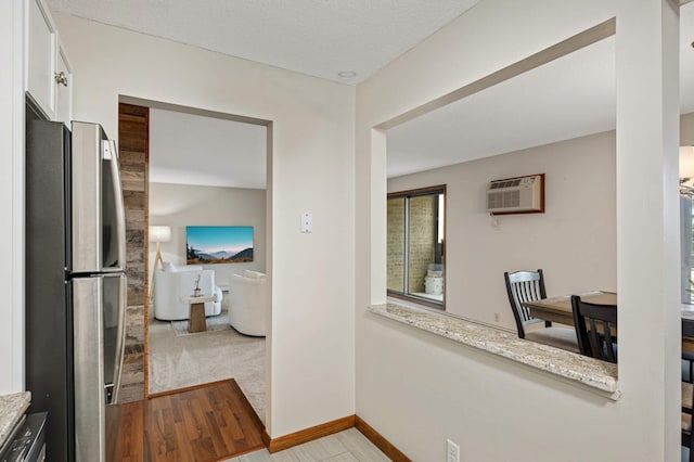 hallway featuring light wood-style flooring, a textured ceiling, an AC wall unit, and baseboards