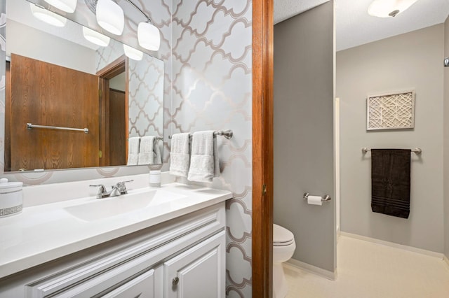 bathroom featuring baseboards, toilet, vanity, and wallpapered walls