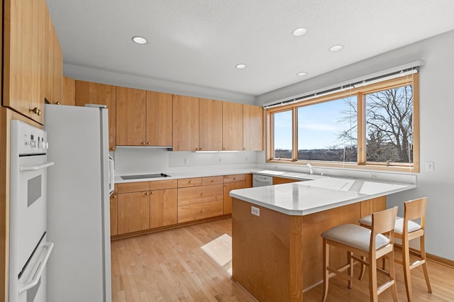 kitchen featuring light wood finished floors, a kitchen breakfast bar, white appliances, a peninsula, and light countertops